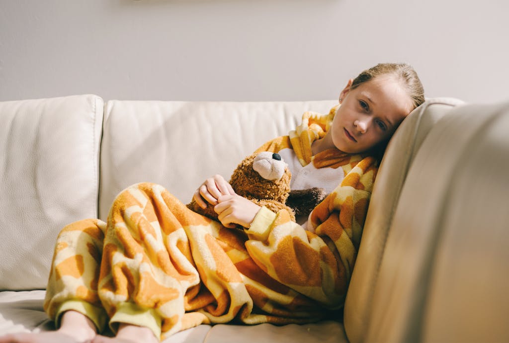 Przeziębione dziecko siedzące w kocu na kanapie, walczące z infekcją Przeziębione dziecko siedzące w kocu na kanapie, walczące z infekcją