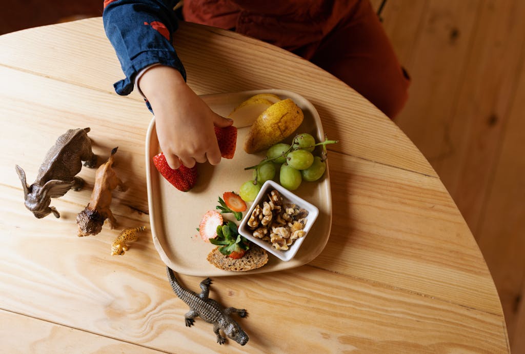 Ręka dziecka sięgająca po owoce leżące na drewnianym stole Ręka dziecka sięgająca po owoce leżące na drewnianym stole
