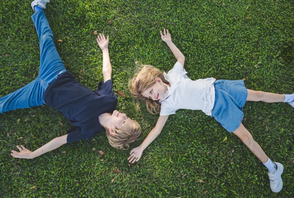 Dzieci leżące na trawie, bawiące się z radością Dzieci leżące na trawie, bawiące się z radością