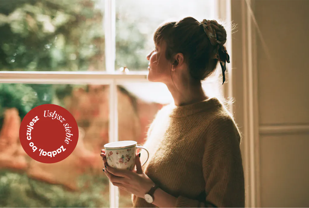 Kobieta z kubkiem herbaty, wyglądająca przez okno