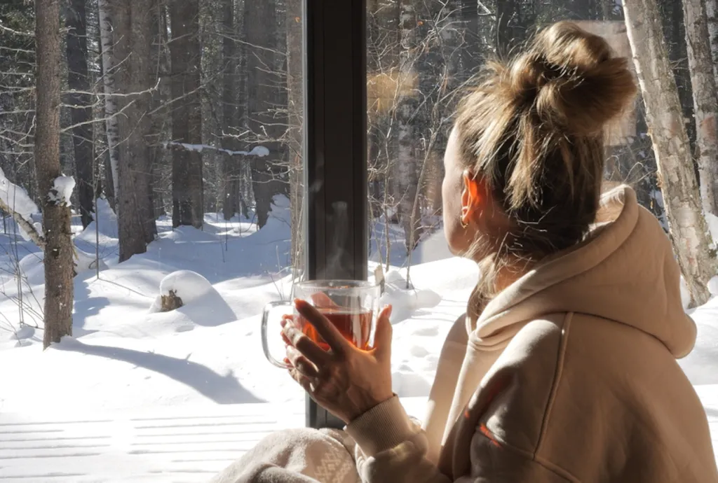Kobieta patrząca za okno podczas zimy, pijąca gorącą herbatę